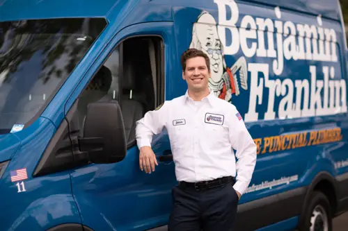 James, a Service Minds Benjamin Franklin Plumbing technician, smiling confidently in front of a Benjamin Franklin Plumbing van in Pompano Beach.